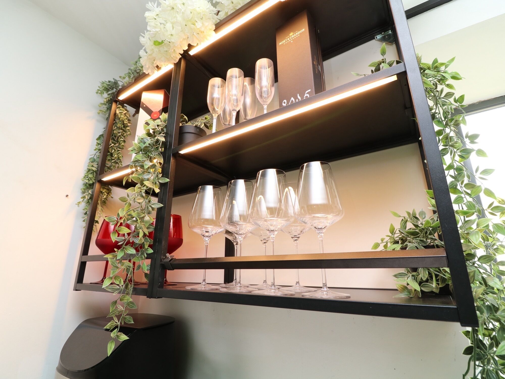 Une étagère murale avec des verres à vin et des plantes décoratives.