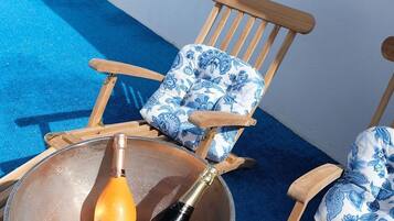 A lounge area with a large metal bowl containing a bottle of champagne, a wooden chair with a floral cushion, and a white table.
