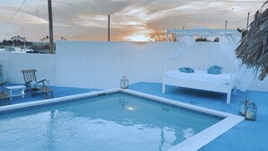 Una piscina amb una cadira de vangat blanca i una taula petita, tot voltat per una paret blava i una palmera.