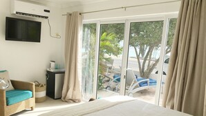 A bedroom with a large bed, a television mounted on the wall, a small desk, and a view of the outdoor area through a sliding glass door.