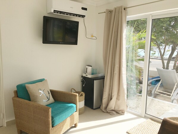 A room with a wicker sofa, a small table with a microwave, and a sliding glass door leading to an outdoor area.