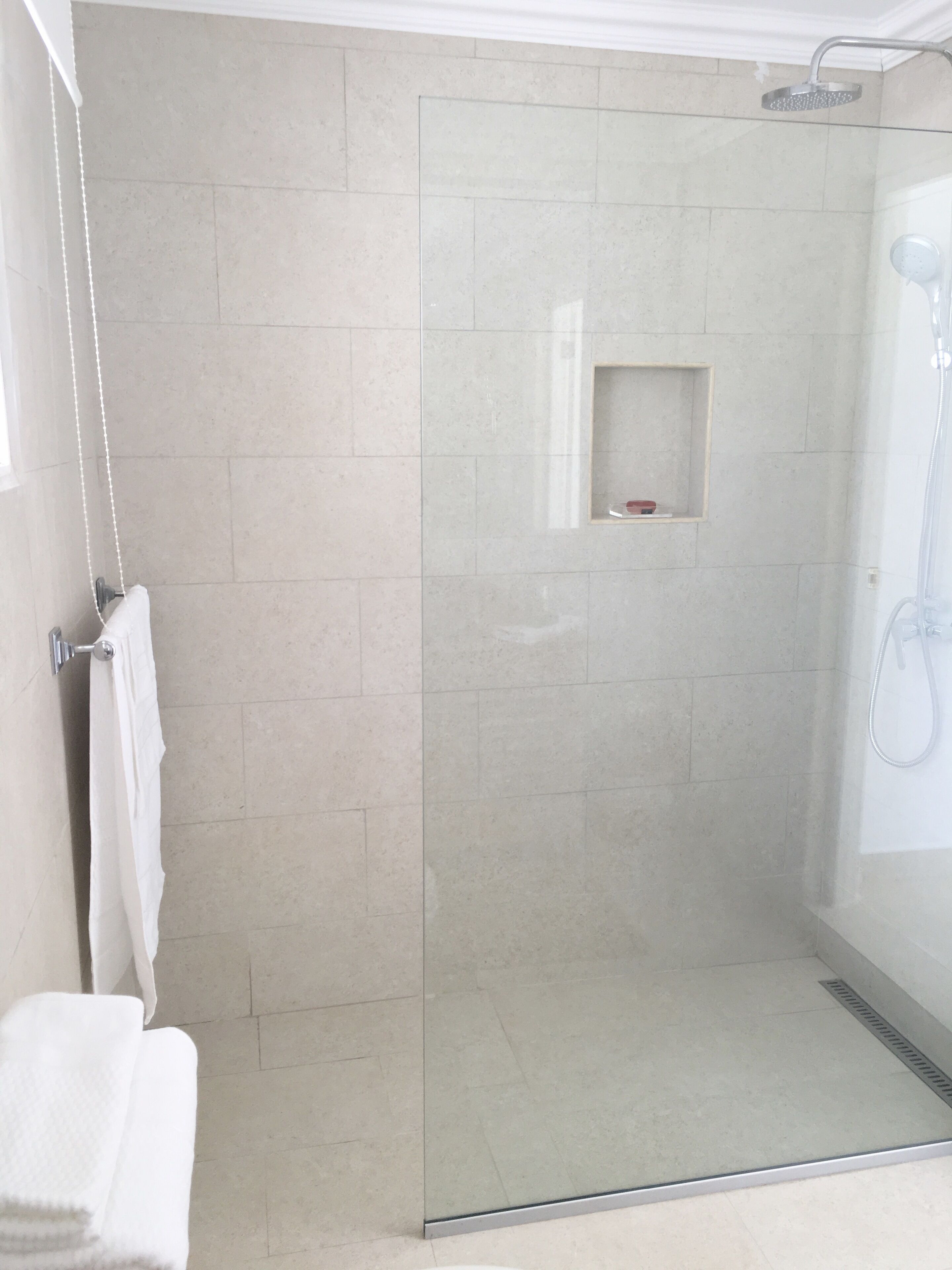 Un espace douche moderne doté d’une porte en verre, d’une petite étagère et d’un porte-serviettes.