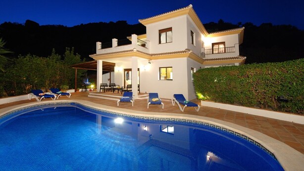 A two-story house with a swimming pool, outdoor seating, and a well-lit balcony.