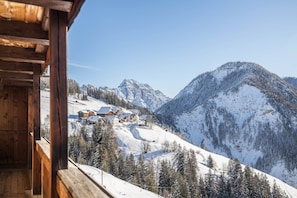 A wooden cabin with a view of a snow-covered mountain and a ski resort.