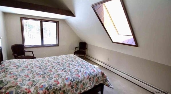 A bedroom with a bed, two chairs, a window, and a skylight.