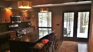 A modern kitchen with a central island, bar stools, and large windows offering a view of the outdoors. - Adirondack “River Rapture"- Lake George/Mount Gore (Warrensburg)