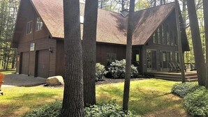 A cabin with a steeply pitched roof, surrounded by tall trees and a well-maintained lawn. - Adirondack “River Rapture"- Lake George/Mount Gore (Warrensburg)