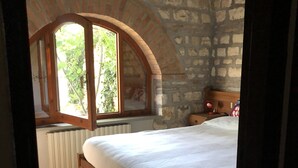 Un dormitorio con pared de piedra, cama de madera, ventana y radiador.