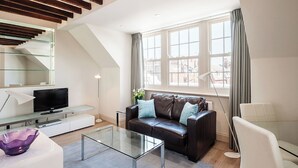 Uma sala de estar moderna com mesa de centro de vidro, sofá de couro e televisão de tela plana sobre um console branco.