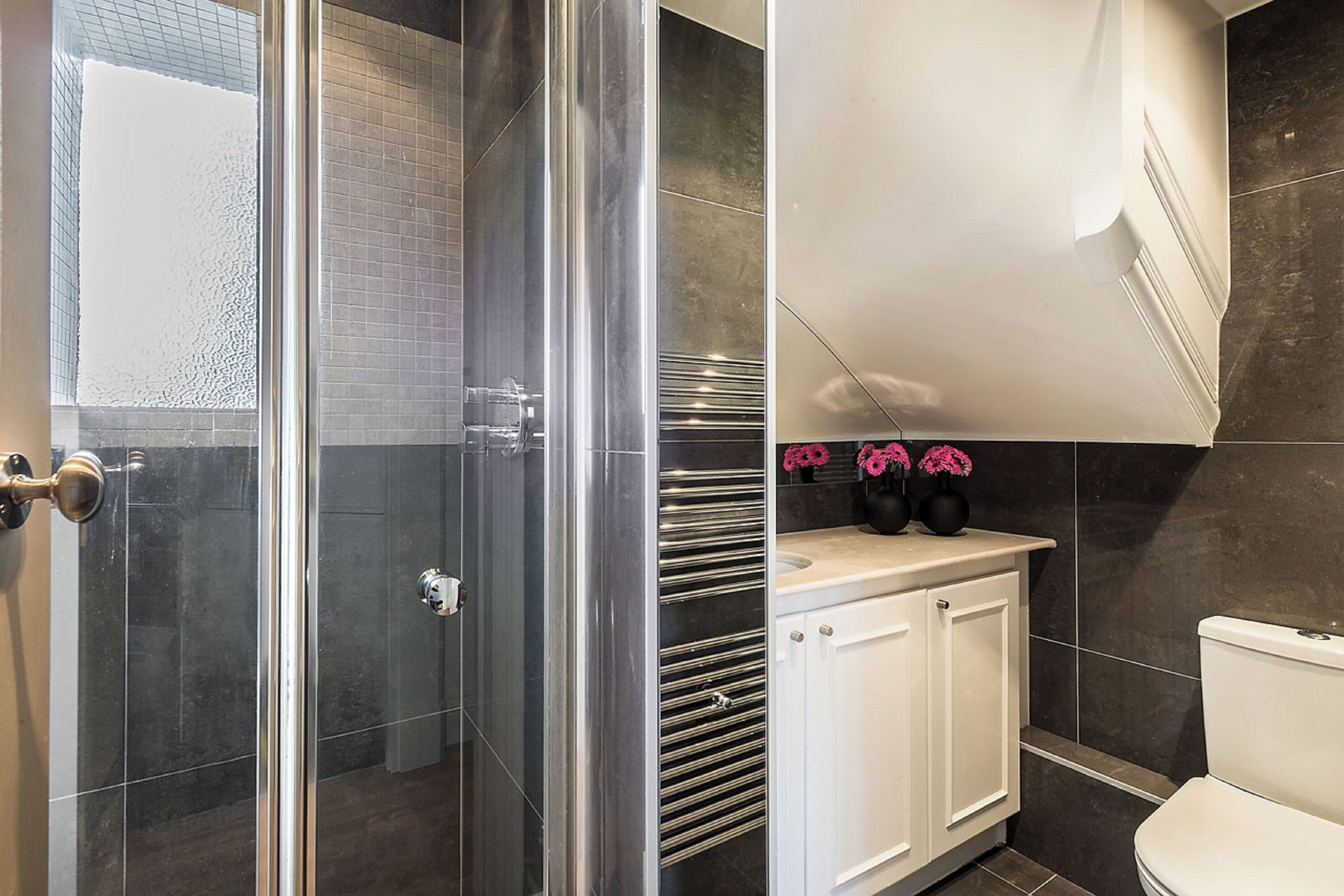 Et moderne badeværelse med en glasbrusekabine, et hvidt toilet og en vask med spejl.