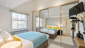 A modern hotel room with two beds, a large mirror, a TV, and a view of the city through the window. - Marylebone - Crawford Street apartments by Viridian Apartments (London)