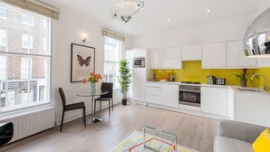 A modern kitchen with white cabinets, a yellow backsplash, and a dining area with a glass table and chairs. - Marylebone - Crawford Street apartments by Viridian Apartments (London)