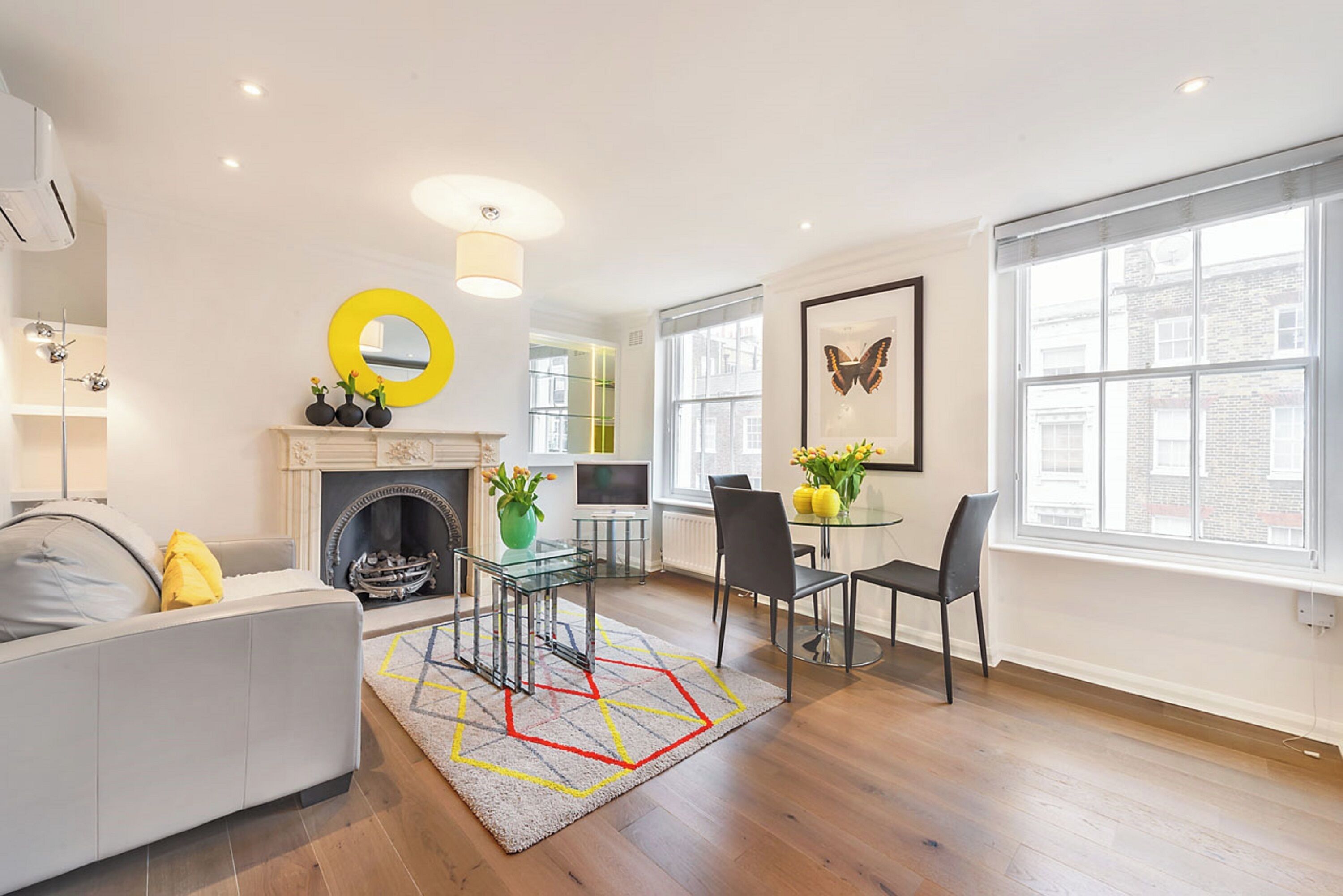 A modern living room with a fireplace, a dining area with a glass table, and large windows providing natural light.