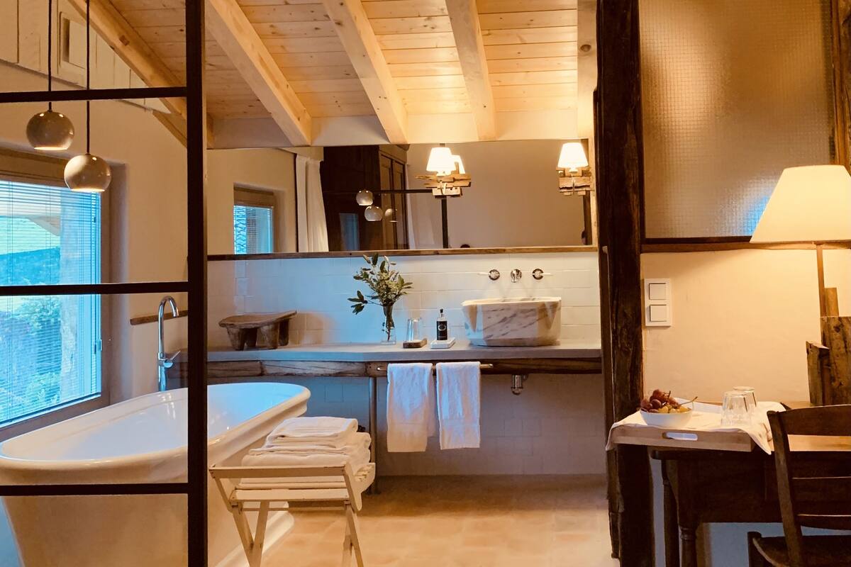 A bathroom with a bathtub, sink, and mirror. There are towels hanging on a rack, and a window providing natural light.