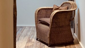 A wicker chair with a cushion in a hallway with wooden flooring and a light fixture on the wall. - OAR Cottage (Garai)