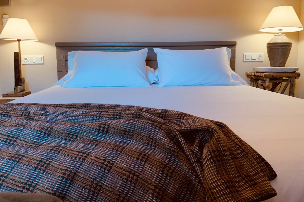 A neatly made bed with white linens, two pillows, and a patterned throw blanket.