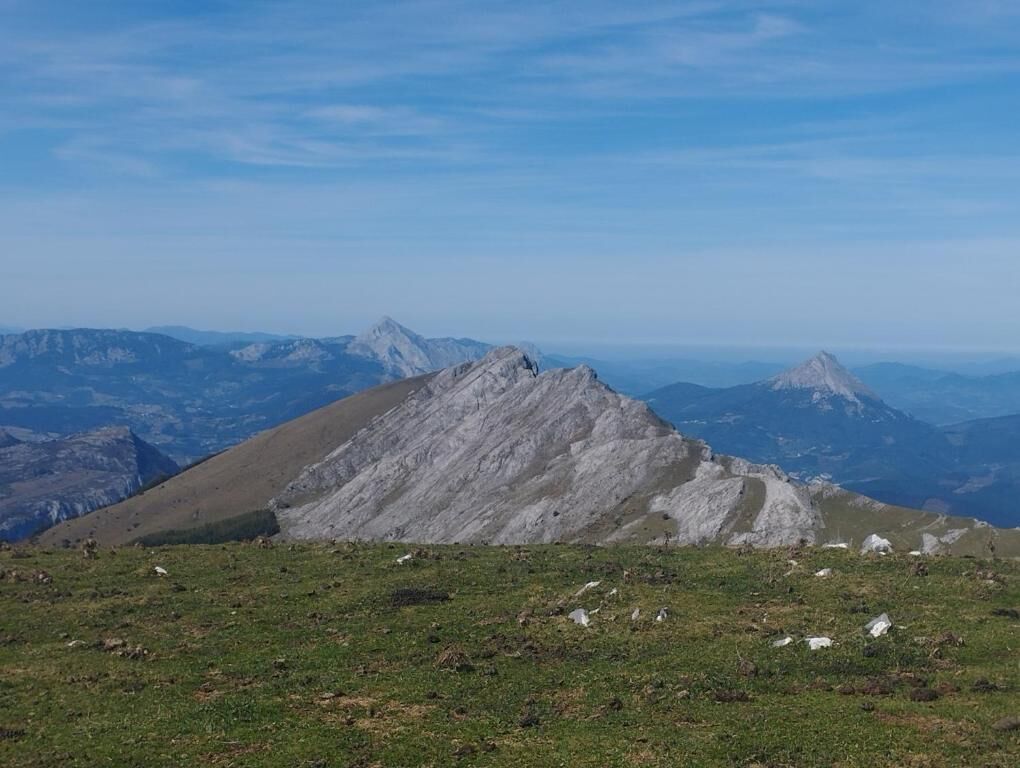 Paisaje montañoso con un pico destacado en primer plano y cordilleras distantes bajo un cielo despejado.