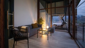 Un salon moderne avec un canapé, une table basse et un fauteuil. Une grande fenêtre offre une vue sur l’extérieur.