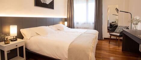 Una habitación de hotel moderna con una cama grande, mesitas de noche, un escritorio y una silla.