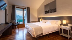 Une chambre d’hôtel comprenant un lit, des tables de chevet, un bureau avec une chaise, une télévision et une grande fenêtre avec des rideaux.