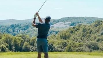 Una persona jugando golf en un campo cubierto de césped, con cielo despejado y colinas al fondo.