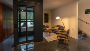 Un hall d’entrée moderne avec une porte d’entrée en verre, un canapé avec des coussins, une lampe sur pied et un escalier.