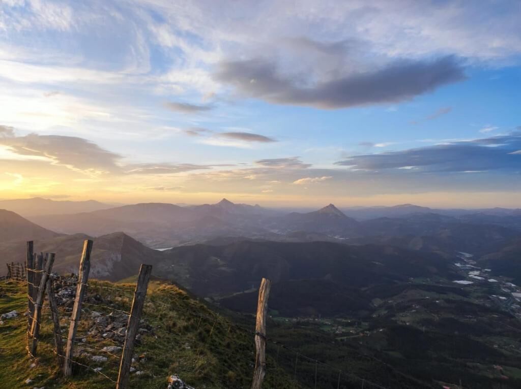 A mountainous landscape with a wooden fence in the foreground and a valley below.