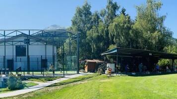 A building with a glass enclosure, a covered outdoor area, and a grassy field.