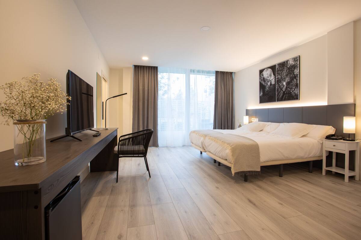Een moderne hotelkamer met een bed, nachtkastje, bureau met televisie en een stoel.