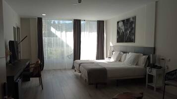 Een hotelkamer met een groot bed, een bureau, een stoel, een televisie en een raam met gordijnen.