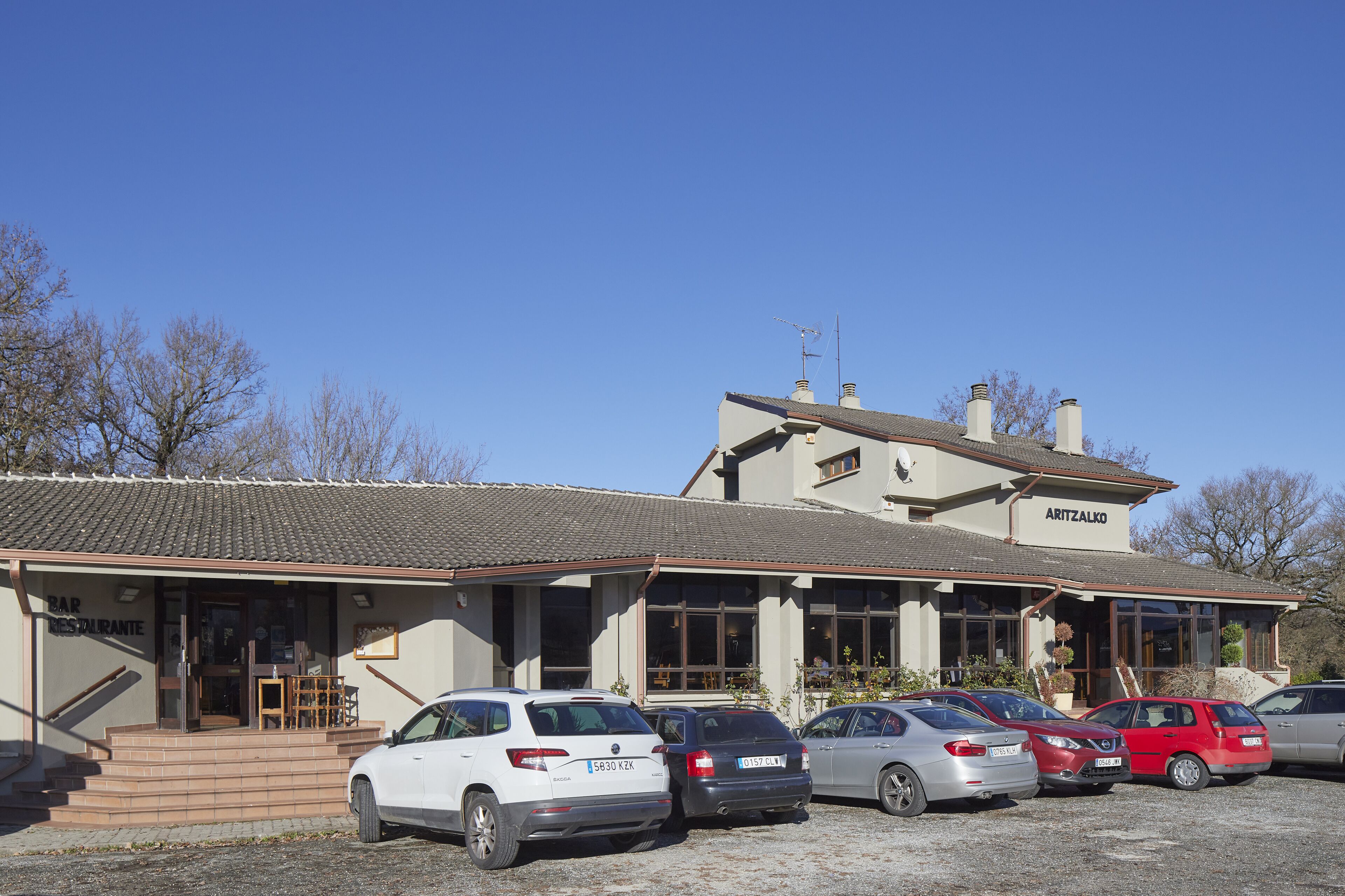 A building with a sign reading "ARITZALKO" and a parking lot with several cars.