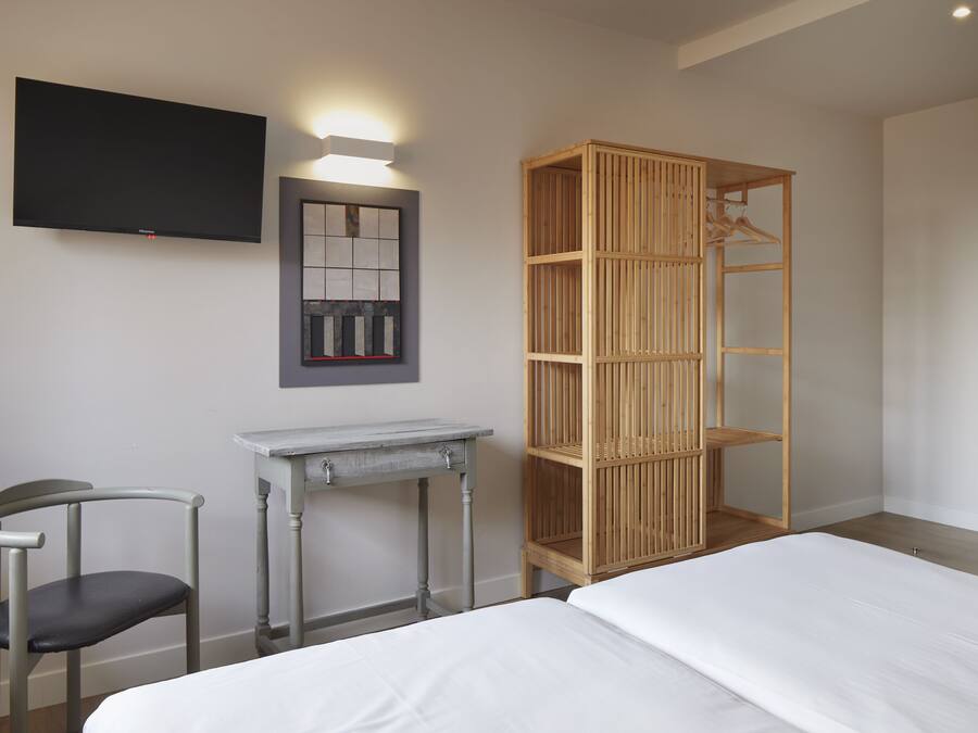 Un dormitorio con cama, escritorio, silla, armario y televisor montado en la pared.