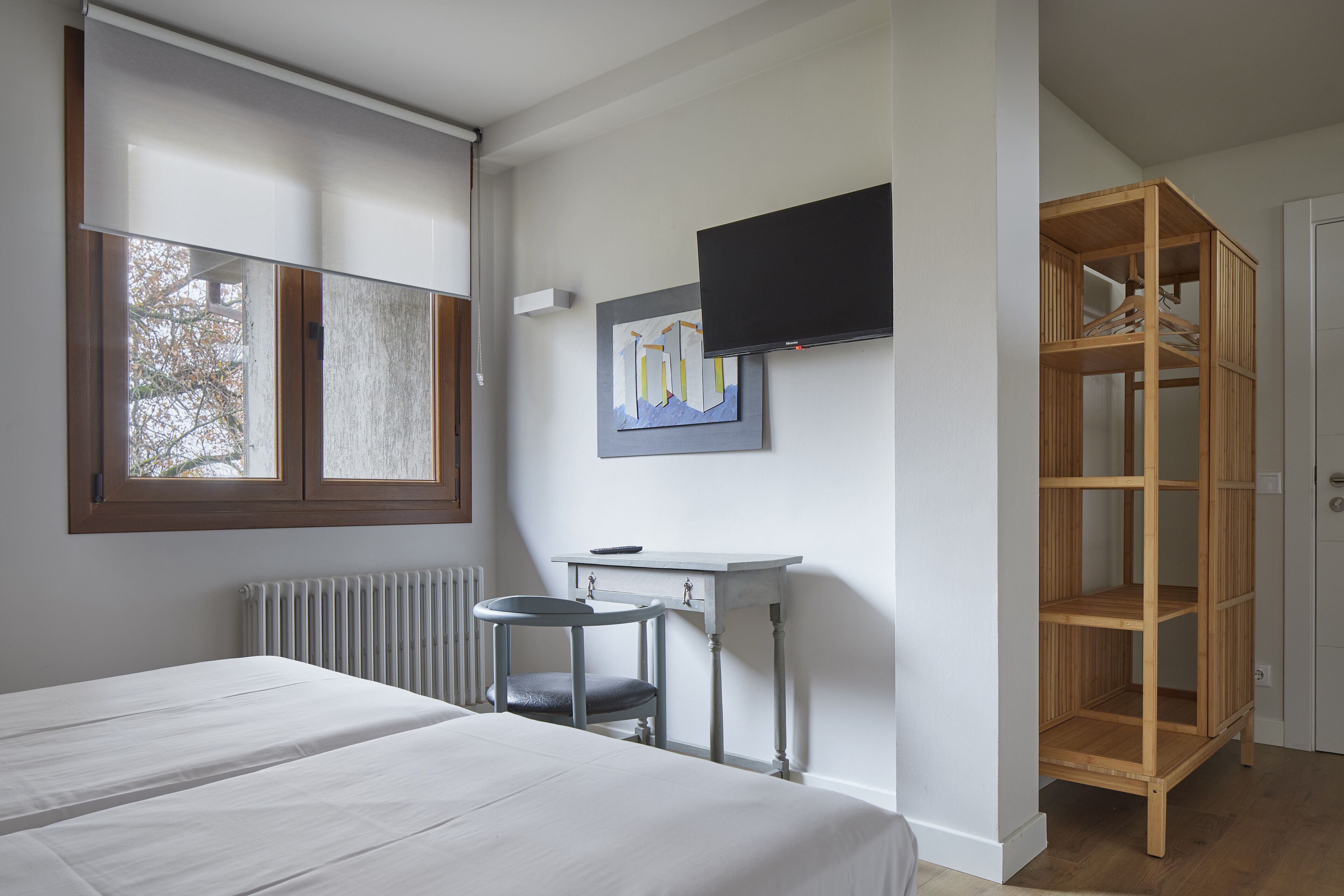 Une chambre à coucher comprenant un lit, un bureau, une chaise, un téléviseur et une étagère en bois.