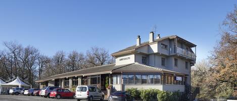 Un edificio de dos pisos con un letrero que dice "APITZALZO". Varias coches están estacionados al frente y un área techada a la izquierda.