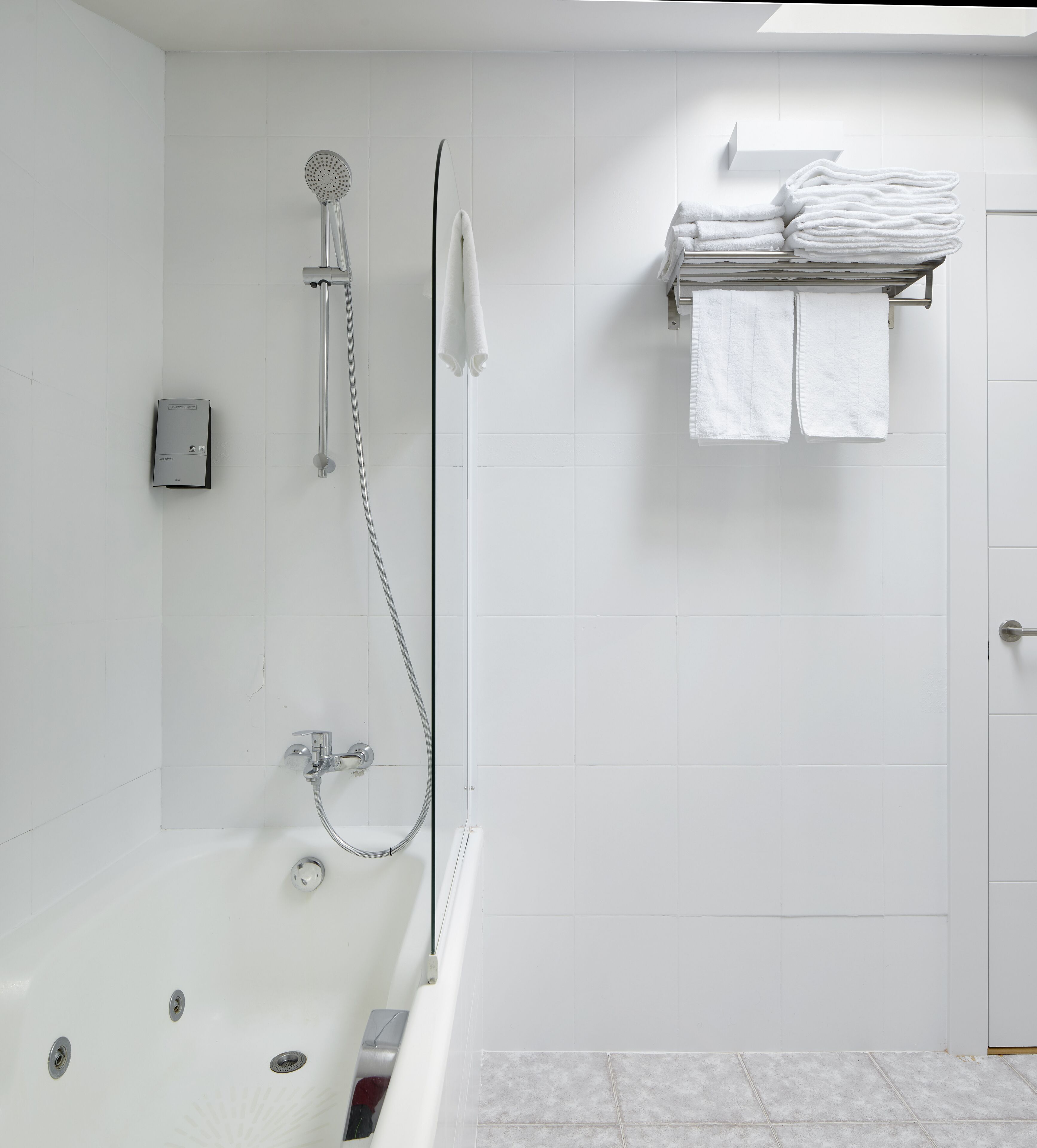 A modern bathroom with a bathtub, a shower with a handheld showerhead, and a stack of neatly folded towels on a shelf.