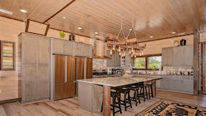 A spacious kitchen with wooden cabinets, a large island with bar stools, and a hanging light fixture. - Friendship Mtn Retreat: : Indoor Pool, Mtn View, Theater, Games, Hot Tub, Wifi (Pigeon Forge)