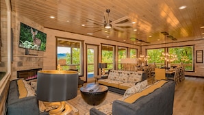 A spacious living room with a fireplace, large windows, a ceiling fan, and a dining area. - Friendship Mtn Retreat: : Indoor Pool, Mtn View, Theater, Games, Hot Tub, Wifi (Pigeon Forge)
