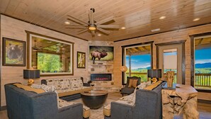 A spacious living room with a stone fireplace, comfortable seating, and large windows offering scenic views. - Friendship Mtn Retreat: : Indoor Pool, Mtn View, Theater, Games, Hot Tub, Wifi (Pigeon Forge)