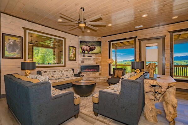 A spacious living room with a stone fireplace, comfortable seating, and large windows offering scenic views.