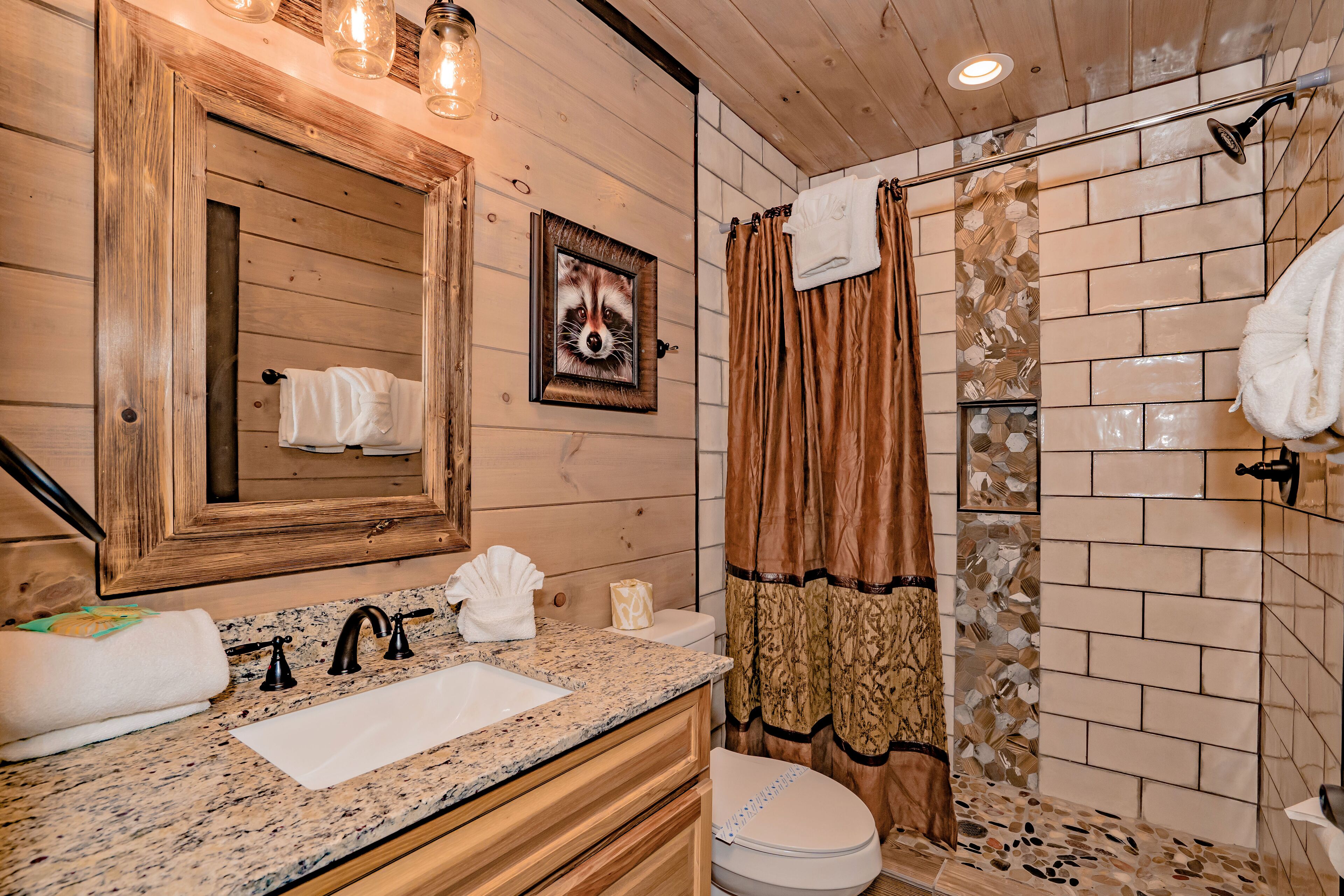 A bathroom with a wooden vanity, a sink, a toilet, and a shower with a patterned curtain.