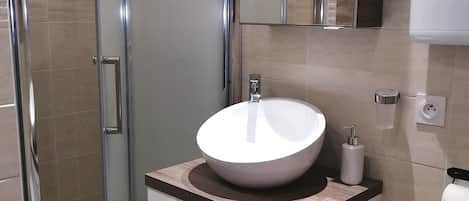 A modern bathroom with a glass-enclosed shower, a white sink with a wooden countertop, and a mirrored cabinet above the sink.