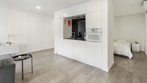 Ett modernt och kompakt bostadsutrymme med ett litet kök, en säng och en liten sittgrupp.