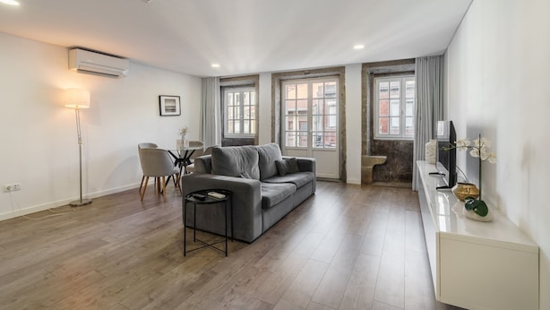 Ett modernt vardagsrum med en grå soffa, ett litet bord, en golvlampa och en tv placerad på en vit tv-bänk.