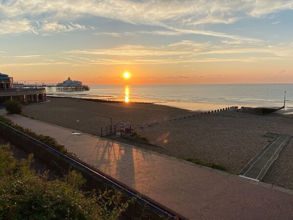 A beach with a sunset, a pier, and a promenade.