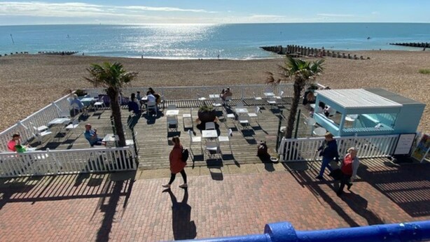 Een terras aan het strand met buitenmeubilair, palmbomen en uitzicht op de oceaan.