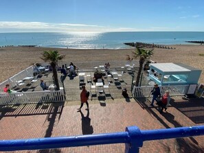 A beachside patio with outdoor seating, palm trees, and a view of the ocean. - Lovely Seaside Apartment in Central Eastbourne (Eastbourne)