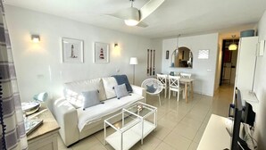 A modern living room with a white sofa, a glass coffee table, a dining area with a white table and chairs, a ceiling fan, and a kitchen visible in the background. - Townhouse with sea view walking distance to the beach - 1 (Mijas Costa)