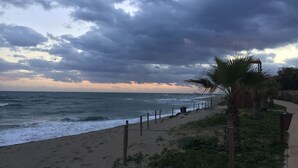 A beach with a wooden fence, palm trees, and a cloudy sky. - Townhouse with sea view walking distance to the beach - 1 (Mijas Costa)