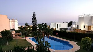 A swimming pool surrounded by greenery, modern buildings, and a clear sky. - Townhouse with sea view walking distance to the beach - 1 (Mijas Costa)