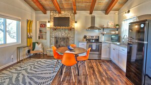 Een moderne keuken met een stenen open haard, houten balken en een eethoek met oranje stoelen.